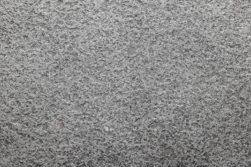 Fototapeta premium A detailed grainy concrete surface. The high-contrast image highlights a rough, porous texture with tiny pebbles and weathered indentations.