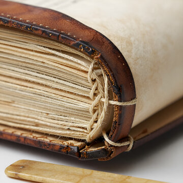A close-up of an open book with a brown leather cover and a close-up of the pages. Hand stitched manuscript binding thread macro.