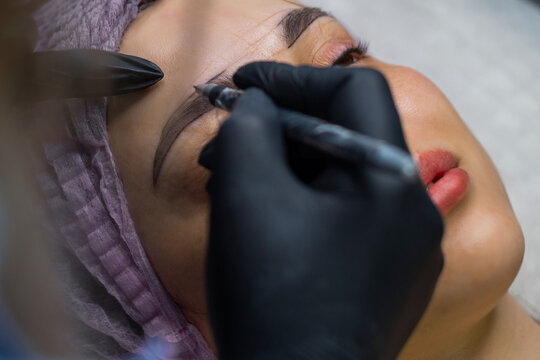 Close up of permanent eyebrow makeup procedure, beautician performing microblading with precision tool in beauty salon