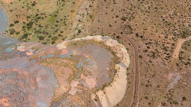 Aerial view of a landscape scarred by earthworks, its layers of ochre, rust, and pale cream cutting through arid scrub, revealing the raw textures of the land, South Africa.