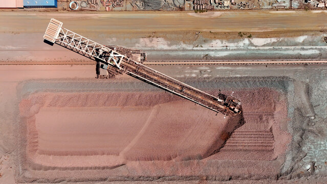 Aerial view of a massive conveyor belt system diligently piling reddish-brown ore, creating a striking contrast against the industrial landscape, Rustenburg, North West, South Africa.