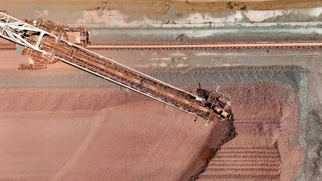 Aerial view of industrial stacker building vast reddish-brown ore pile, showcasing stark, textured earth, Rustenburg, North West, South Africa.