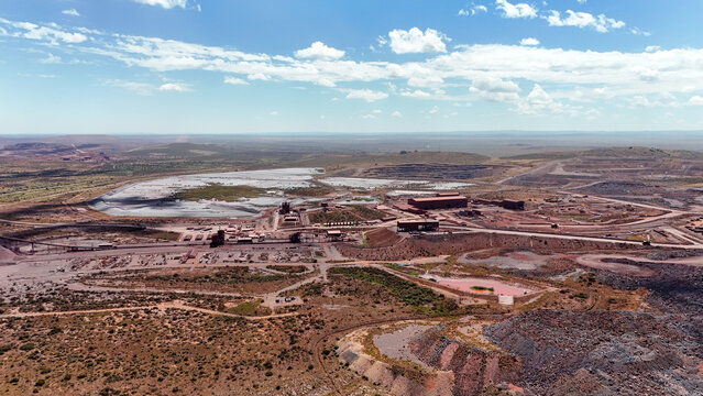 Aerial view of a sprawling industrial mining complex, with vast reddish-brown earth and shimmering water bodies under a clear sky, Rustenburg, North West, South Africa.