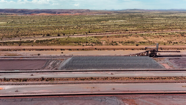 Aerial view of gray aggregate piles and industrial conveyors on red earth, contrasting with the rugged landscape, Rustenburg, North West, South Africa.