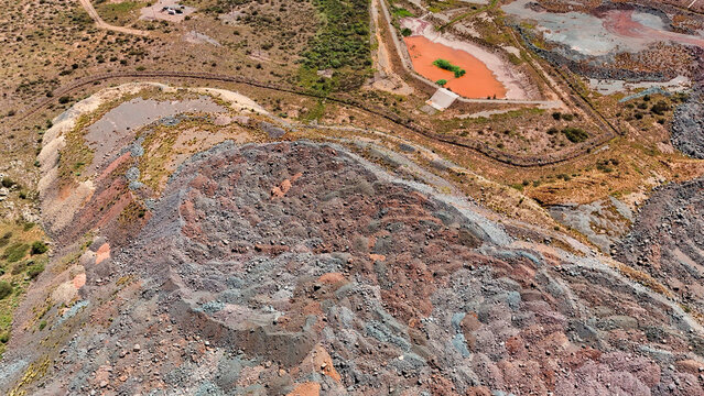 Aerial view of a striking industrial landscape where layered earth in hues of rust and grey meets a vivid orange reservoir, Rustenburg, North West, South Africa.