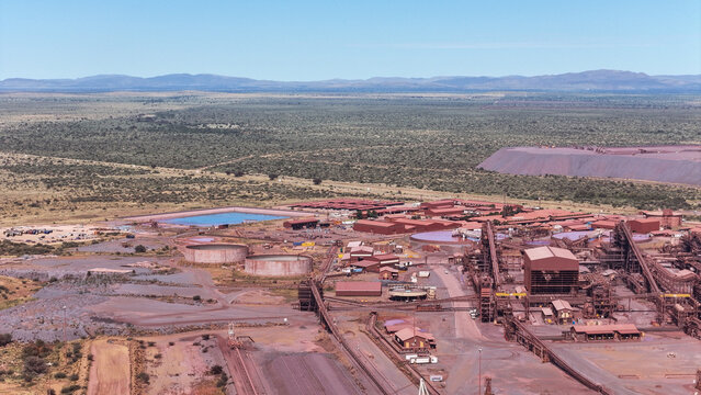 Aerial view of a sprawling industrial mining complex with vast reddish-brown earthworks and processing facilities amidst green bushveld, Rustenburg, North West, South Africa.