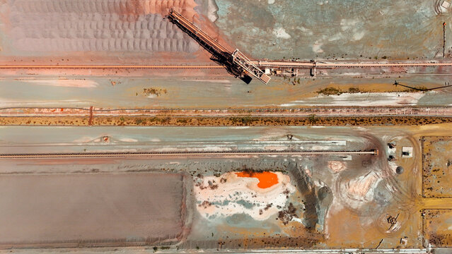 Aerial view of a sprawling industrial site with a conveyor belt, vibrant orange pools, and diverse earth tones, Rustenburg, North West, South Africa.