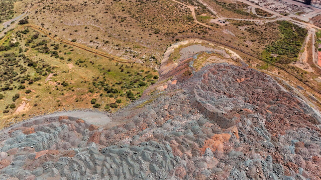 Aerial view of a vast, multi-hued mine dump, its textured grey and reddish strata contrasting with the arid, sparse land, Rustenburg, North West, South Africa.