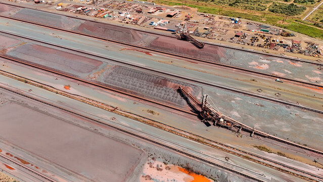 Aerial view of vast industrial landscape with rich russet earth mounds and powerful ore handling machinery under a bright sky, Rustenburg, North West, South Africa.
