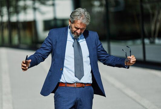 Portrait of a happy smart inteligent senior businessman smiling using a phone smartphone standing in the front of the office building