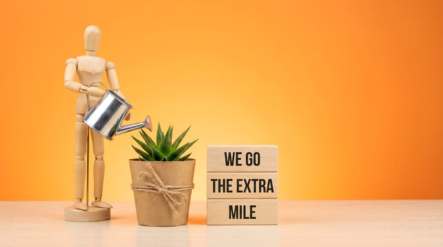 We go the extra mile motivational text on wooden blocks with mannequin watering plant for service and business growth