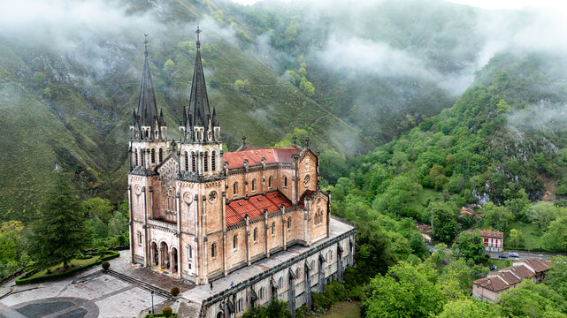 Aerial view of the Basilica's spires piercing the misty mountain air, a symphony of stone and nature's embrace, Basilica de Santa Maria la Real de Covadonga, Cangas de Onis, Spain.
