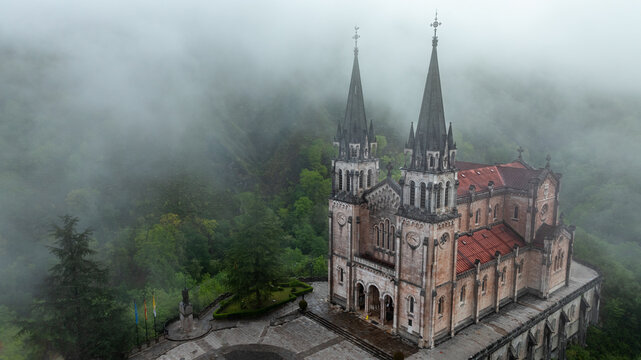 Aerial view of the Basilica de Santa Maria la Real de Covadonga piercing through the ethereal mist, a symphony of stone and sky, Basilica de Santa Maria la Real de Covadonga, Cangas de Onis, Spain.