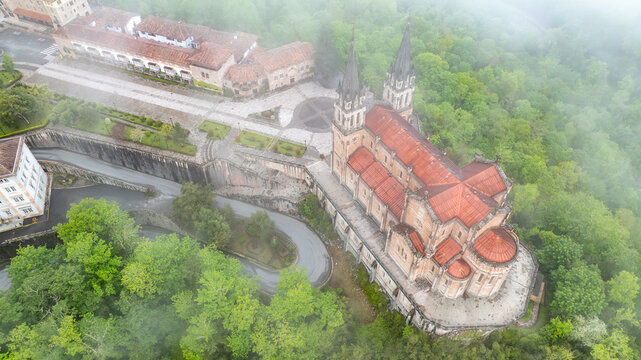 Aerial view of the Basilica de Santa Maria la Real de Covadonga stands majestically amidst lush greenery, its red-tiled roof contrasting with the verdant landscape, Cangas de Onis, Spain.