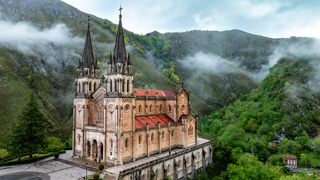 Aerial view of the Santa Maria la Real de Covadonga Basilica stands majestically against a backdrop of verdant mountains veiled in ethereal mist, Cangas de Onis, Spain.