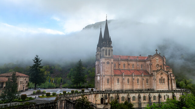 Aerial view of the Basilica's spires pierce through the mist, a fusion of gothic majesty and ethereal serenity, Basilica de Santa Maria la Real de Covadonga, Cangas de Onis, Spain.