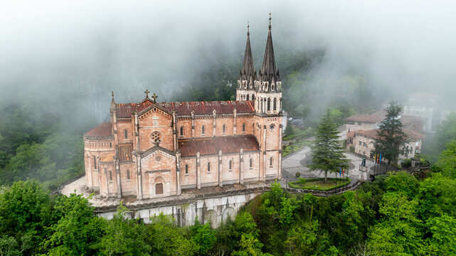Aerial view of the majestic Basilica de Santa Maria la Real de Covadonga rises from the verdant landscape, shrouded in ethereal mist, Cangas de Onis, Spain.