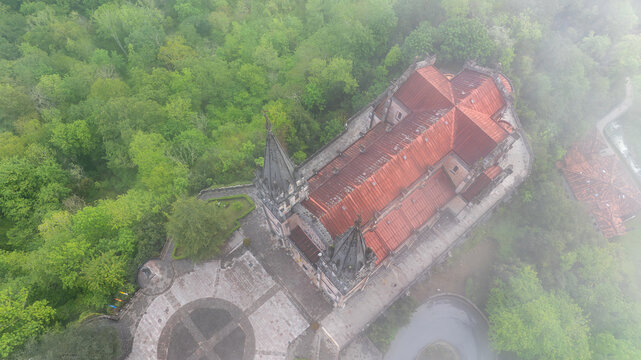 Aerial view of the Basilica de Santa Maria la Real de Covadonga emerges from the mist-shrouded mountain, its red tiled roof contrasting with the verdant canopy, Cangas de Onis, Spain.