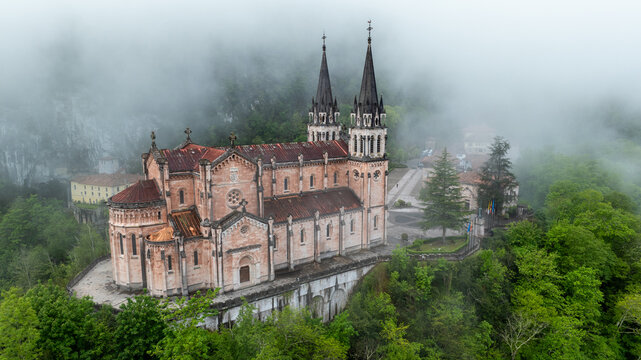 Aerial view of the Basilica of Santa Maria la Real de Covadonga shrouded in mist, its spires piercing the ethereal fog, Cangas de Onis, Spain.