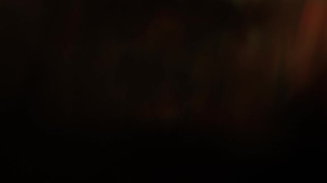 Real warm golden light leak with soft amber bokeh sweeping across dark background. Organic optical lens flare transition overlay for cinematic music video intro and title sequence.