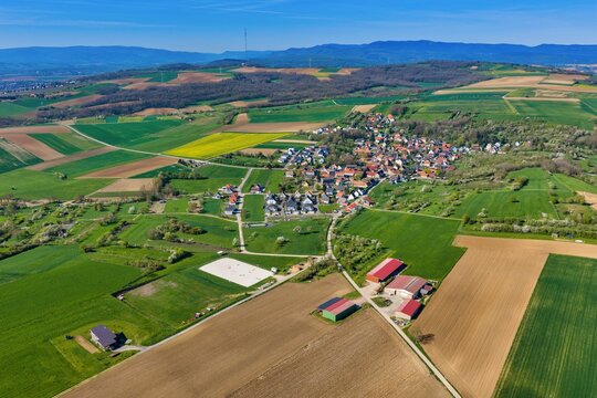 Aerial view of a small village surrounded by a vivid tapestry of green fields and brown tilled earth, Wintzenheim-Kochersberg, Grand Est, France.