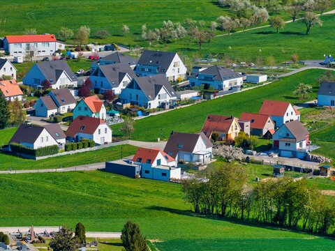 Aerial view of a cluster of homes with contrasting rooftops amidst vibrant green rolling hills, Wintzenheim-Kochersberg, Grand Est, France.