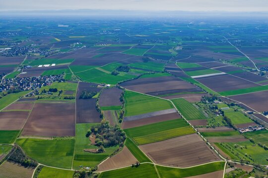 Aerial view of contrasting brown and green fields, a village, and scattered trees under a bright sky, Wintzenheim-Kochersberg, Grand Est, France.