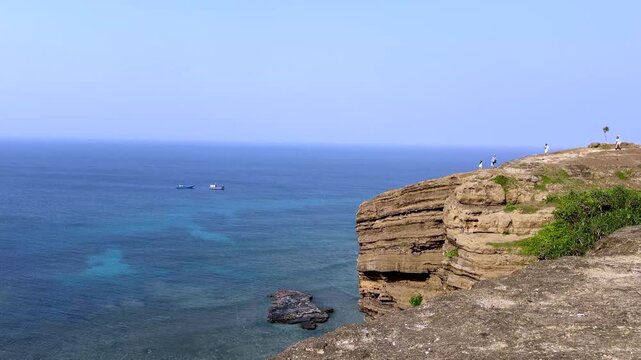Tourists on rocky coastal cliff overlooking blue ocean, Ly Son Island Vietnam scenic seascape