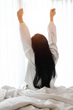 A vertical shot of a young woman stretching in bed as she wakes up to the warm morning sunlight. represents a fresh start, restful sleep, positive mental health, and relaxed morning lifestyle.