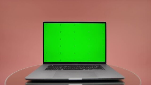 Laptop with green screen mockup on table on pink
