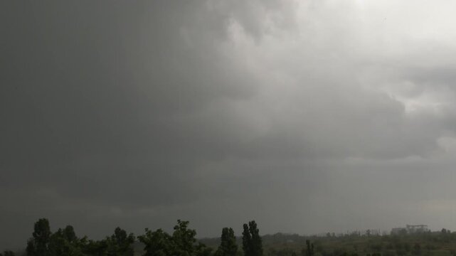 Powerful lightning strikes horizon through gray clouds in severe thunderstorm sky.