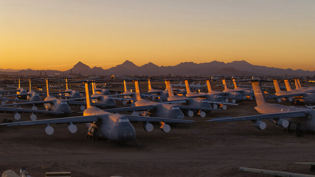 Tucson, United States - 06 February 2025: Aerial view of retired military aircraft gleaming under a dramatic desert sunset, casting long shadows across the boneyard with mountains beyond.