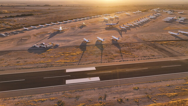 Tucson, United States - 30 November 2025: Aerial view of a vast aircraft boneyard under a golden sunset, casting long, stark shadows across the arid, sandy terrain.