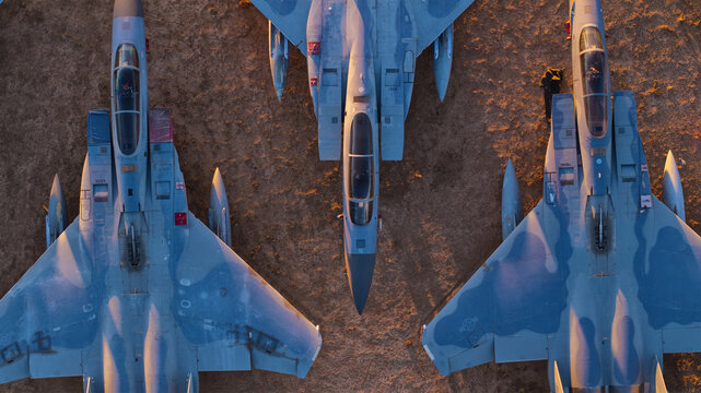 Tucson, United States - 06 February 2025: Aerial view of sleek military fighter jets, their blue-grey camouflage stark against the warm, golden-brown earthen canvas at sunset.