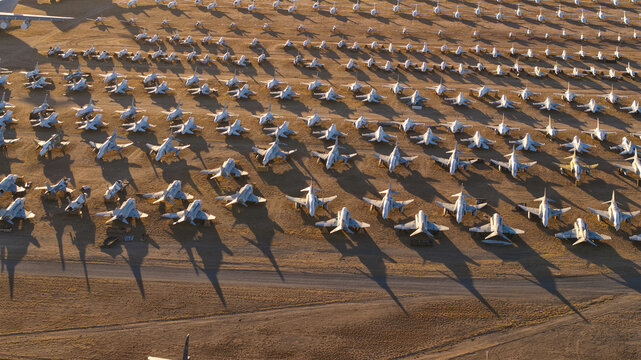 Tucson, United States - 06 February 2025: Aerial view of countless retired aircraft, stark white against the ochre desert, lined in silent, shadowed rows.