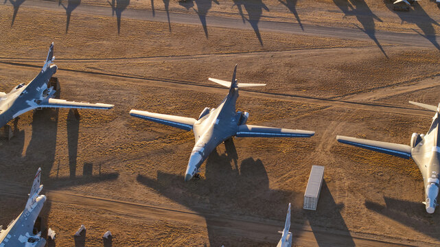 Tucson, United States - 06 February 2025: Aerial view of numerous grey warbirds resting on the vast, ochre desert floor, casting long, stark shadows under the golden light.