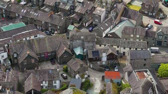 A close orbital aerial shot over the densely packed slate rooftops and winding lanes of Ambleside town centre, Cumbria, showcasing its distinctive stone architecture.