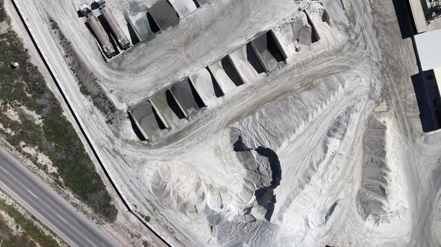 A tracking drone shot from a top-down angle moving over a gravel production site, showing trucks and large aggregate piles near the Lorca mountains.