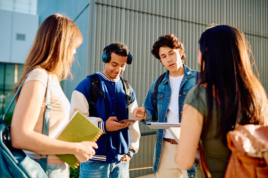 Group of diverse university students communicating and collaborating on campus, using a digital tablet and mobile phone outdoors
