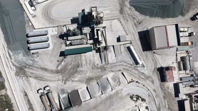 A tracking drone shot from a top-down perspective flying over an asphalt plant and gravel factory with complex industrial machinery and silos.