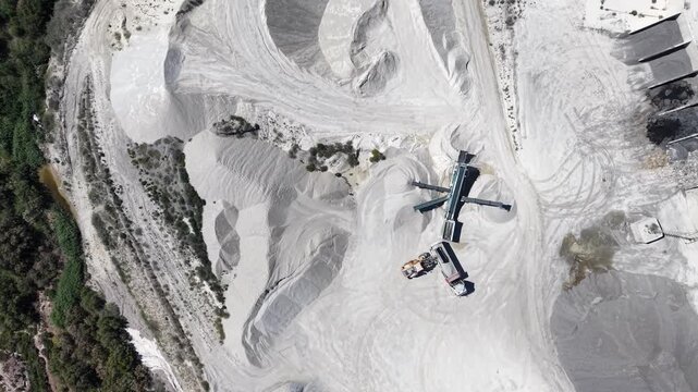 A tracking drone shot from a top-down perspective showing a gravel business with massive piles of aggregate, trucks, and processing machinery.