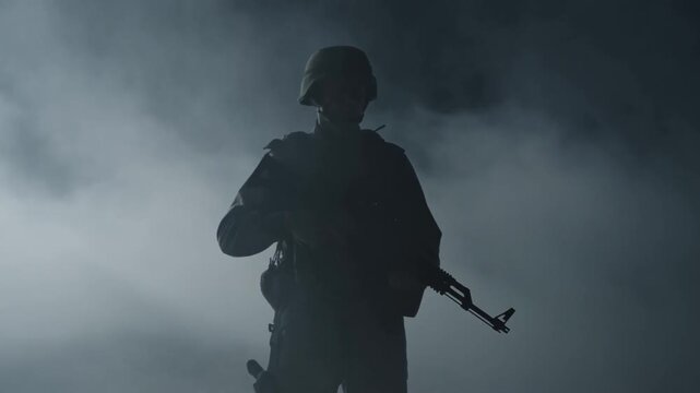 Tracking shot of soldier silhouette emerging through thick smoke holding rifle on foggy battlefield frontline at dawn