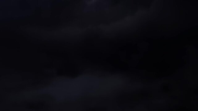 Time lapse pan of storm clouds rolling across night sky above dark horizon with slow sweeping motion and layered cloud formations