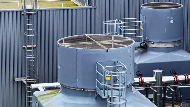 Close-up view of industrial cooling towers and metal ladders against a corrugated metal wall. Ideal for manufacturing or industrial process visuals.