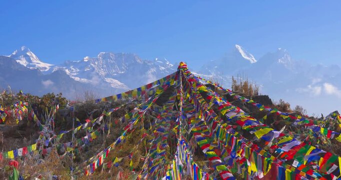 From Ama Yangri showing colorful prayer flags spread across hills with Langtang snow-capped peaks rising under a clear blue sky in Nepal.