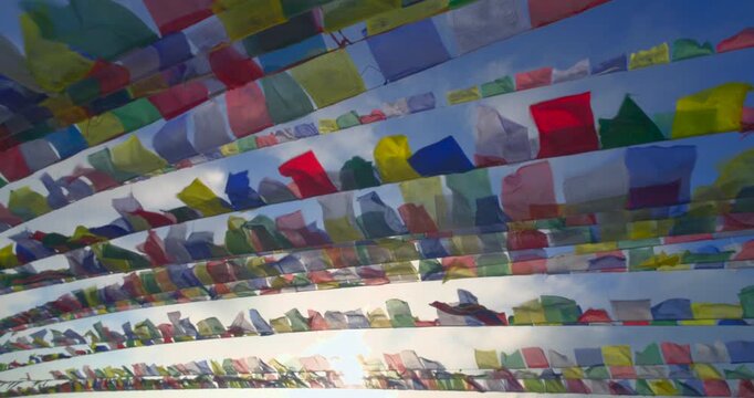 Prayer flags at Ama Yangri, Nepal glowing as sunlight passes through the flags while they move gently against soft clouds and a clear blue sky.