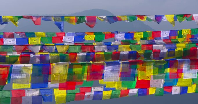 Rows of colorful prayer flags with sacred symbols stretching across the frame with a misty blue mountain ridge under a pale sky at Ama Yangri Nepal.