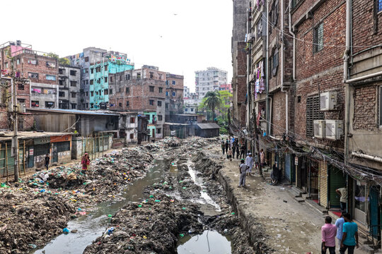 Keraniganj, Bangladesh - 11 April 2026: Aerial view of a stark, garbage-choked canal winding through densely packed, weathered urban dwellings under a muted sky.