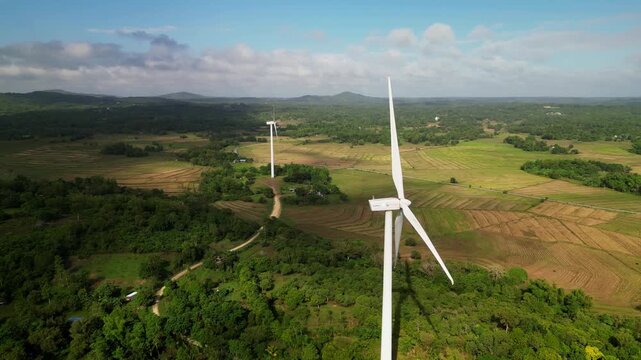 Aerial orbit of wind turbines rising above farmland and forest landscape in Guimaras Island, Philippines during daytime