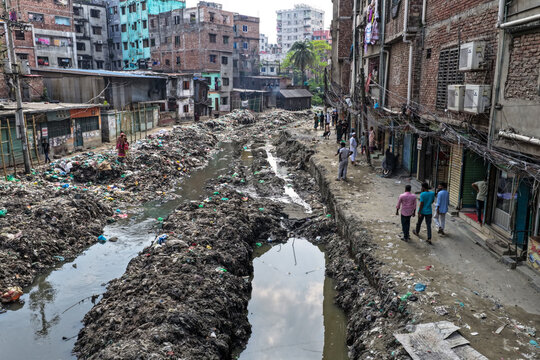 Keraniganj, Bangladesh - 11 April 2026: Aerial view of a severely polluted urban canal, mounded with dark refuse, flanked by worn brick buildings and bustling paths.